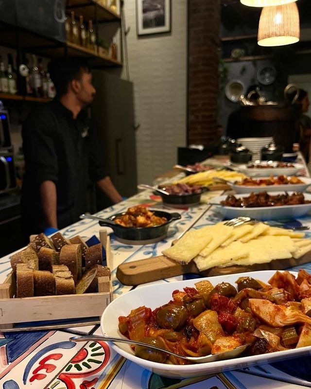 Un tavolo sormontato da piatti di cibo e un uomo in piedi dietro di esso.
