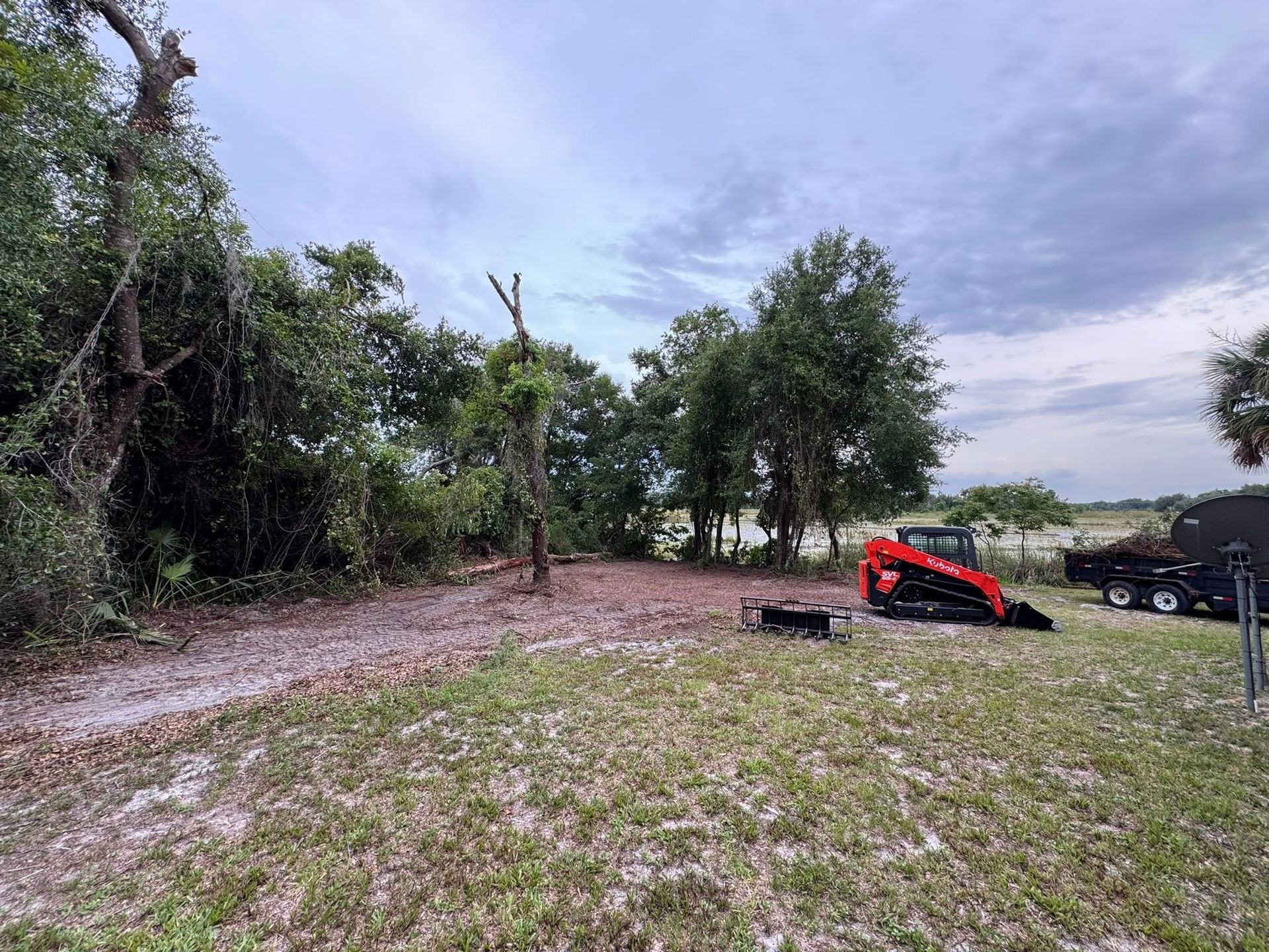 Rural yard with trees, a red tractor, and a black pickup truck under a cloudy sky.