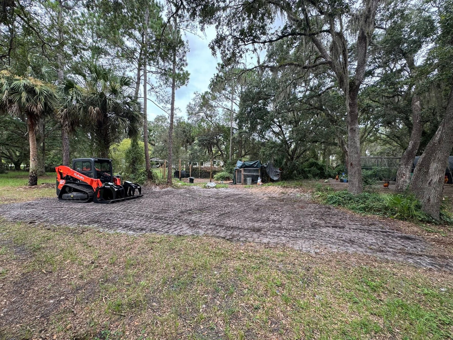 Orange tractor in a wooded clearing with gravel and trees around it