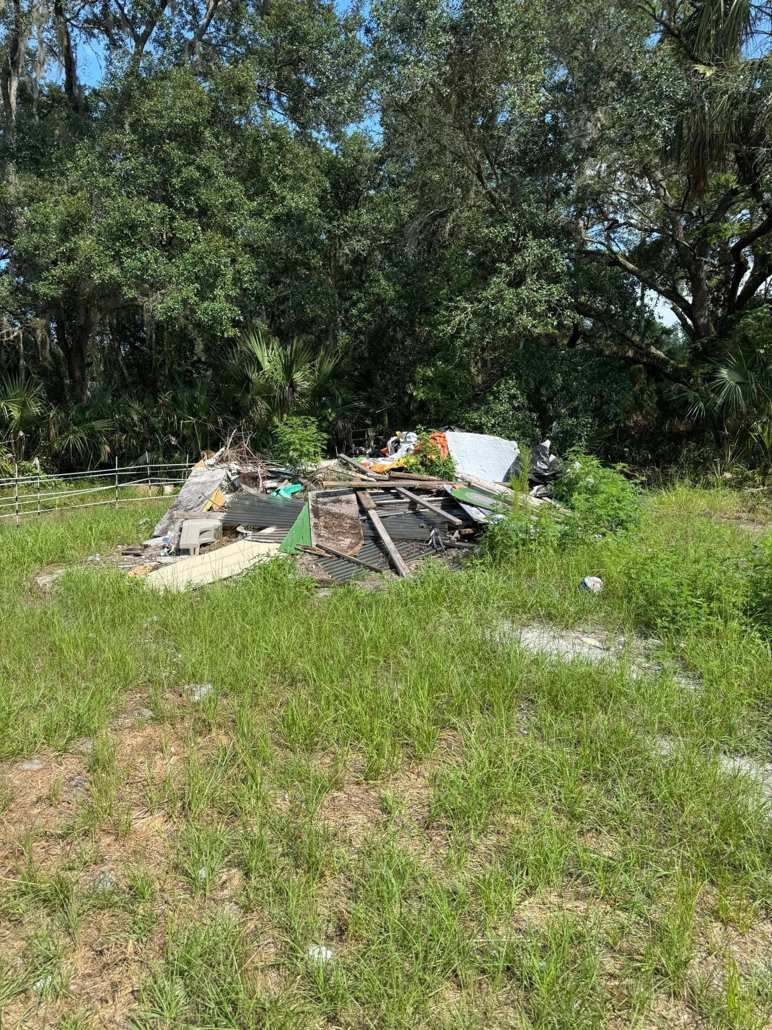 Trash pile in a grassy clearing beside trees and brush