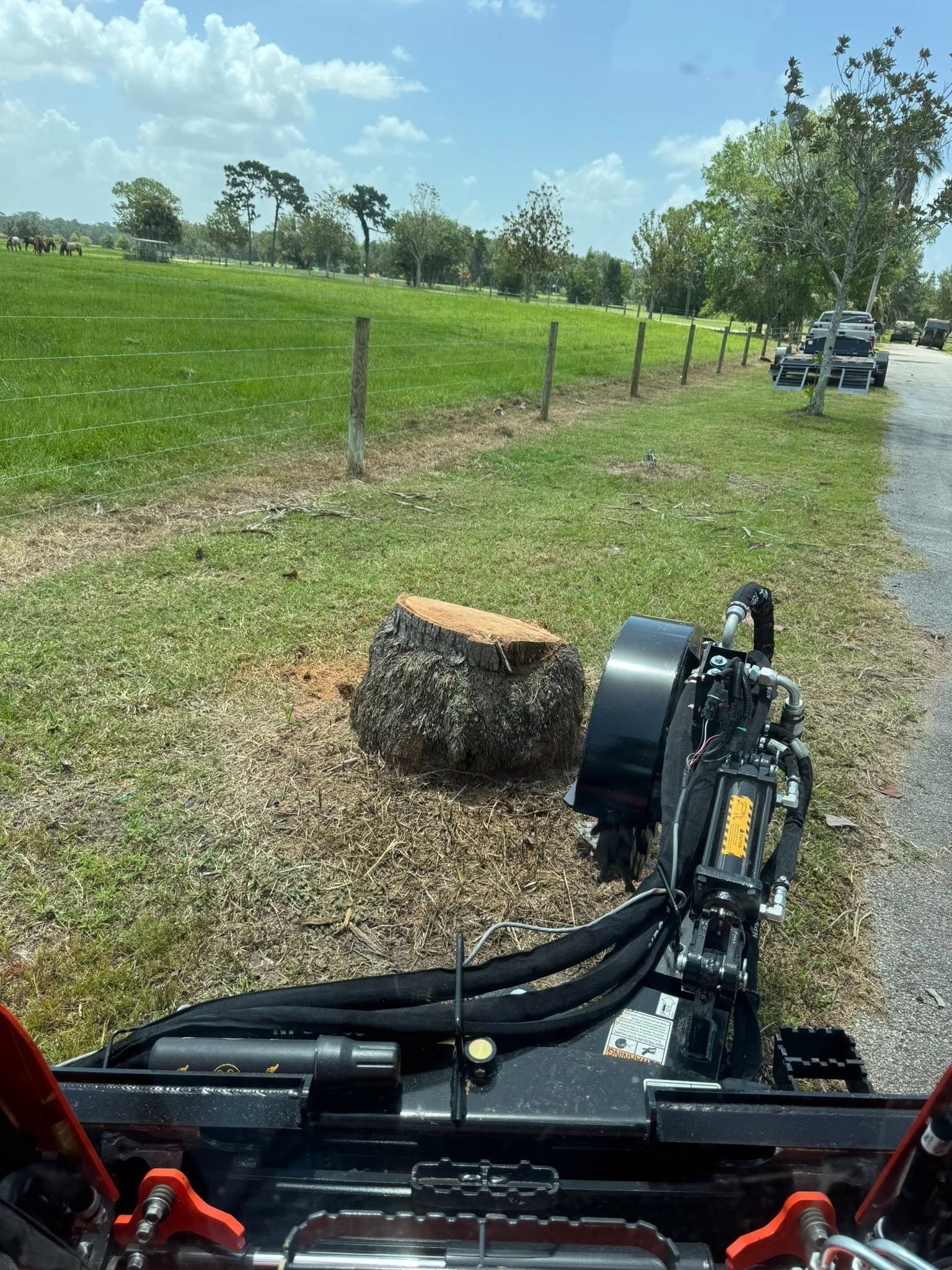Tractor mower beside a grassy field, cutting near a fence on a sunny rural roadside.