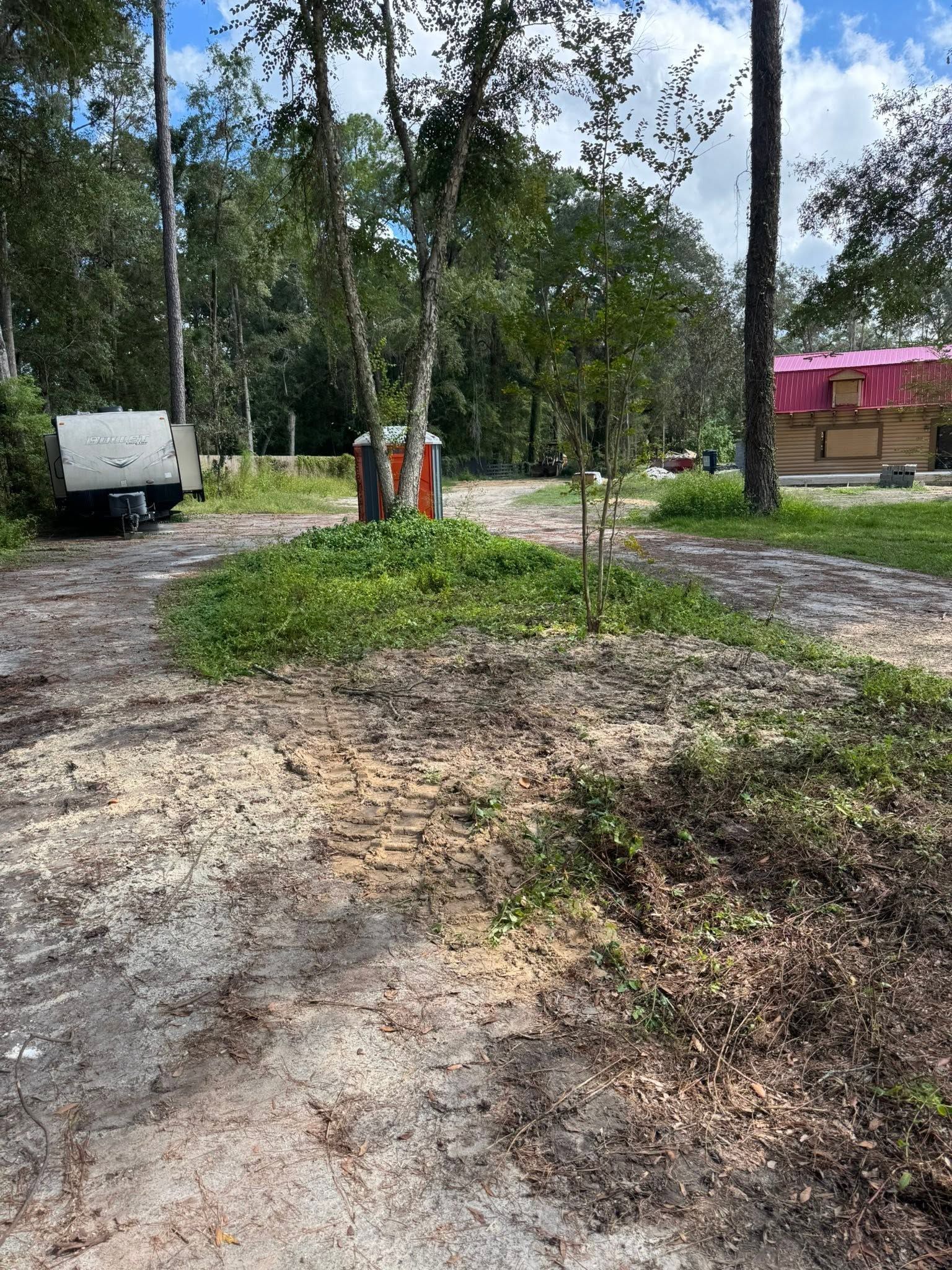Tree-lined dirt path with a white van, utility equipment, and a pink-roofed building in the background