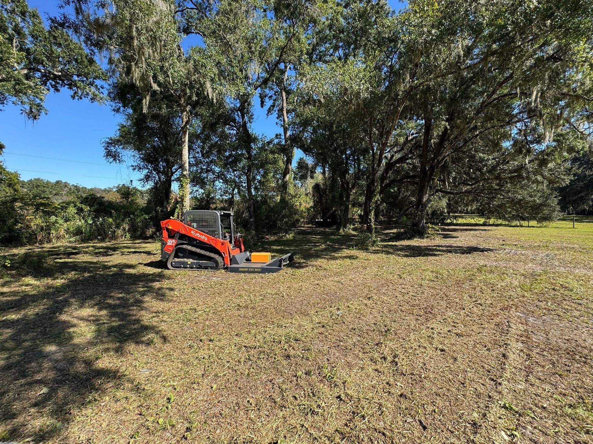 Orange lawn mower in a grassy yard near trees under a clear blue sky