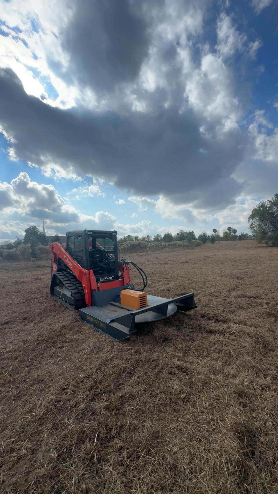 Red compact tractor with front attachment in a dry field under a cloudy sky