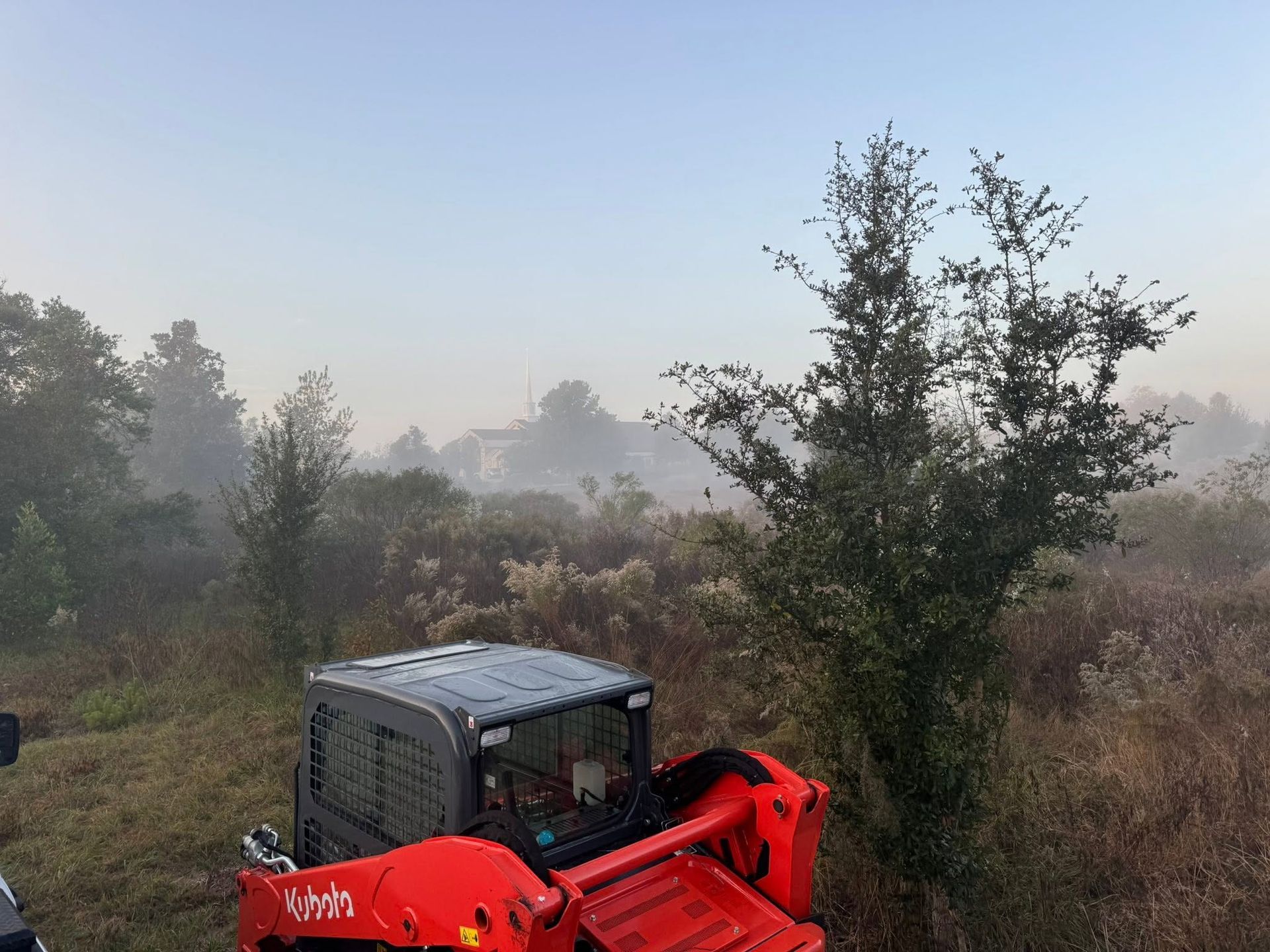 Red tractor in a misty field with trees at dawn
