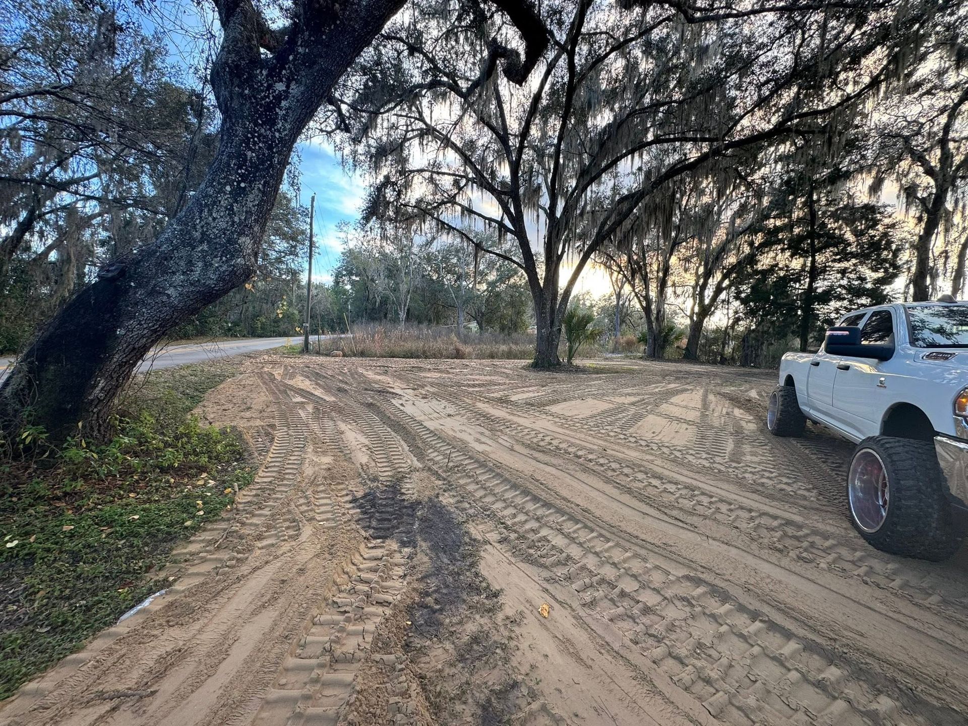 Sandy dirt road through trees at dusk, with a white off-road vehicle parked on the right.