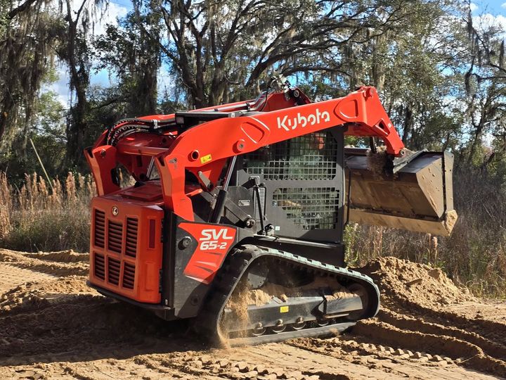 Orange Kubota compact track loader digging dirt in a wooded area.