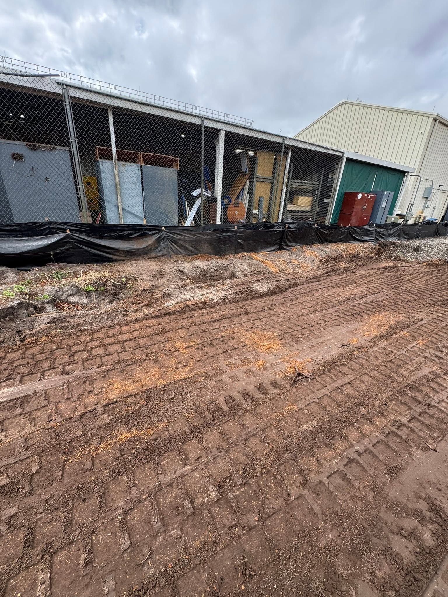 Mud-covered construction site with a damaged building, chain-link fence, and overcast sky