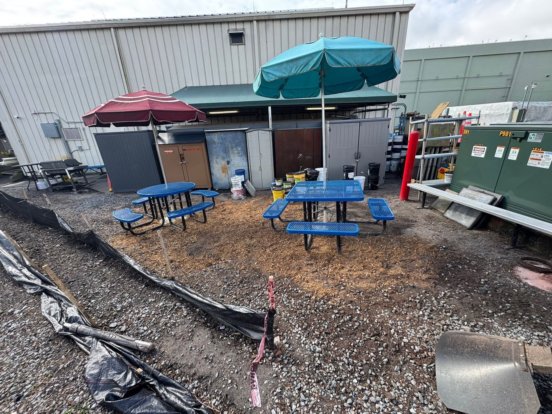 Outdoor patio with blue tables, red and teal umbrellas, and equipment beside a building