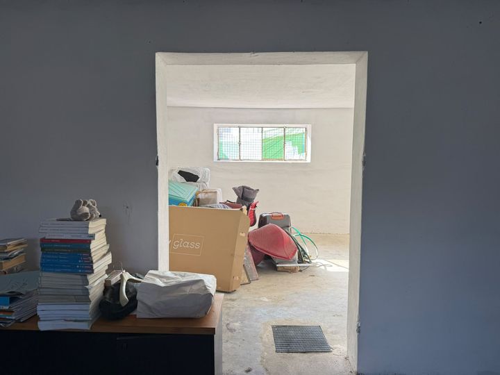 Stanza vuota con pareti blu, una porta che dà su un ambiente disordinato e materiali impilati sulla sinistra.