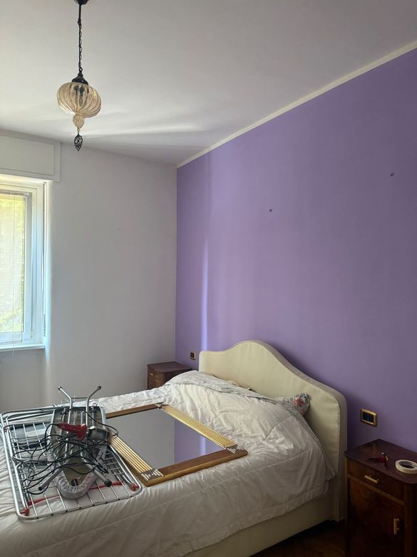 Camera da letto con una parete d’accento viola, un letto color crema, comodini e una lampada a sospensione.