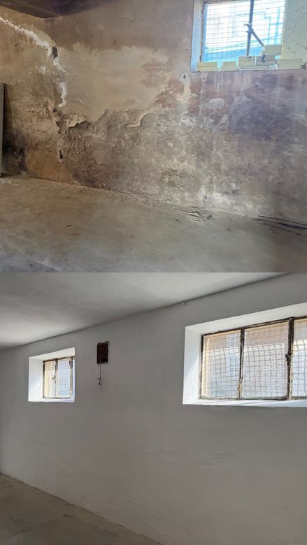 Parete interna e soffitto danneggiati, con intonaco che si scrosta, crepe e due piccole finestre da cui entra la luce