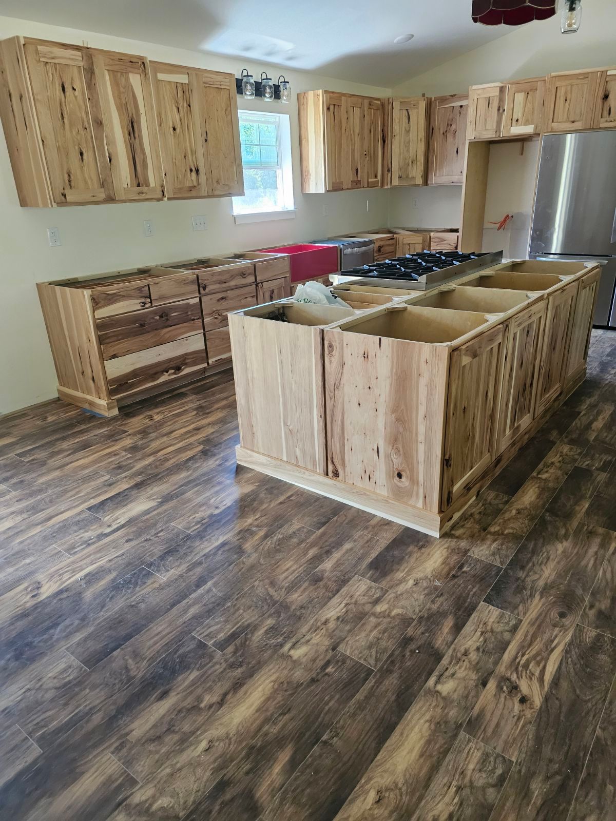 Unfinished kitchen with wood cabinets, island, and flooring; appliances not installed.
