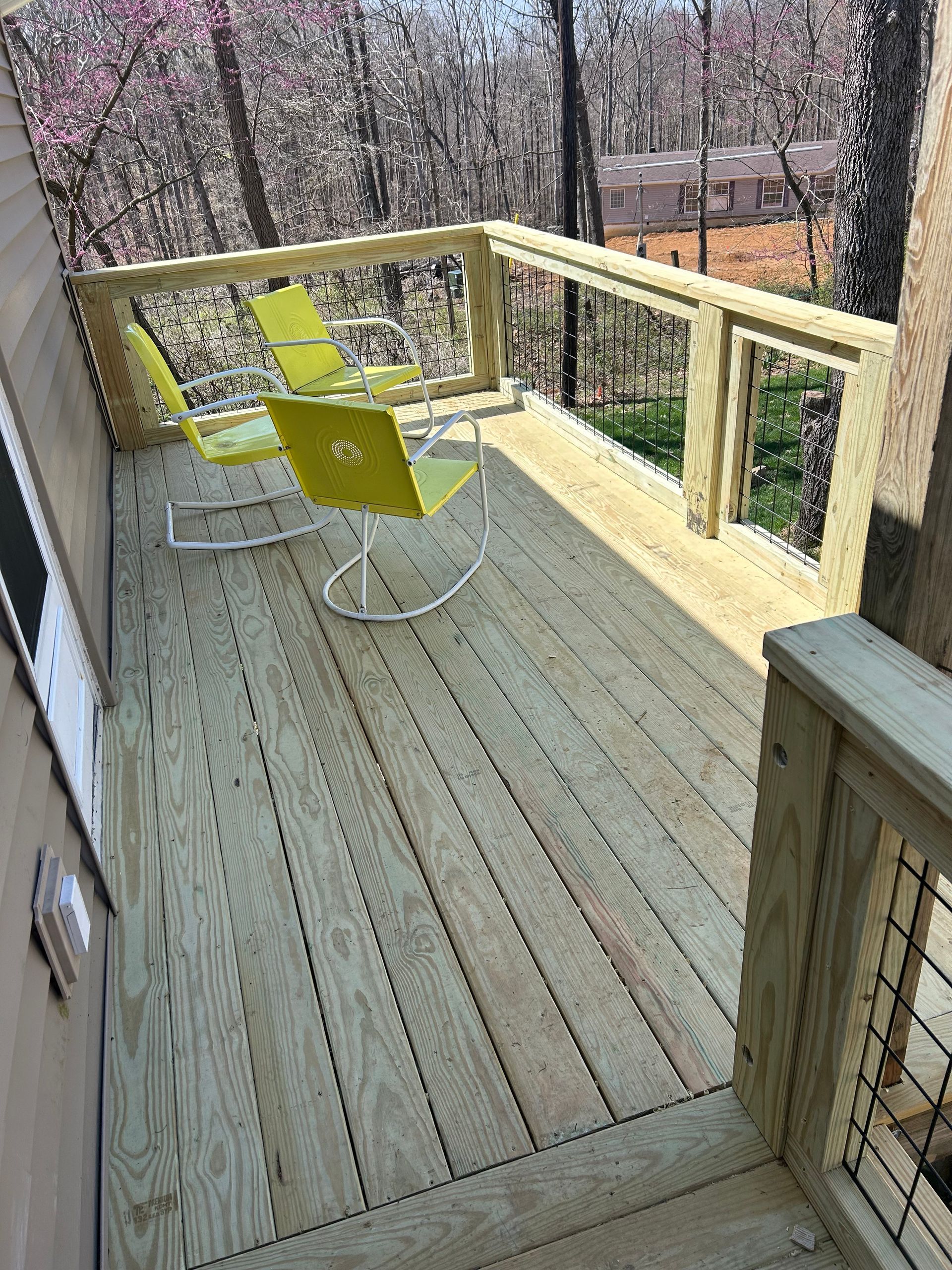Two lime green rocking chairs on a wooden deck overlooking a forest.