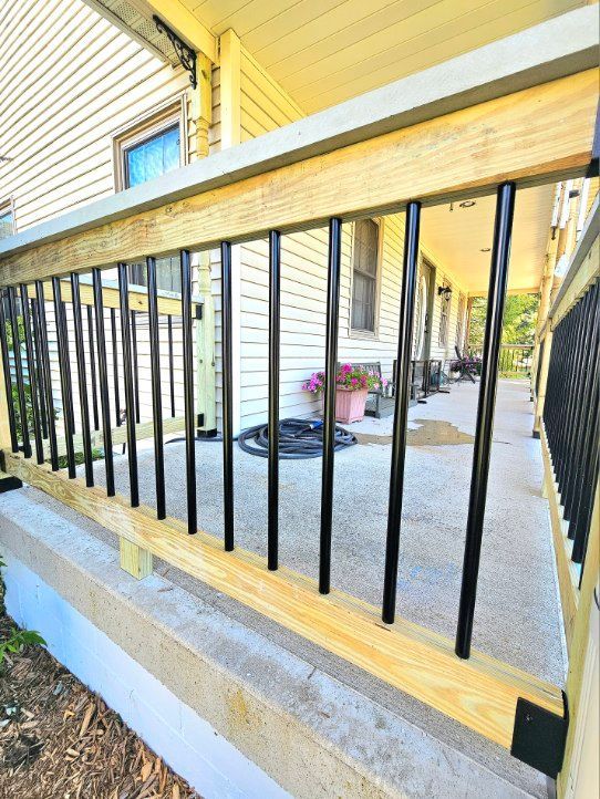 A wooden porch railing with vertical black metal balusters set against a light yellow house exterior.