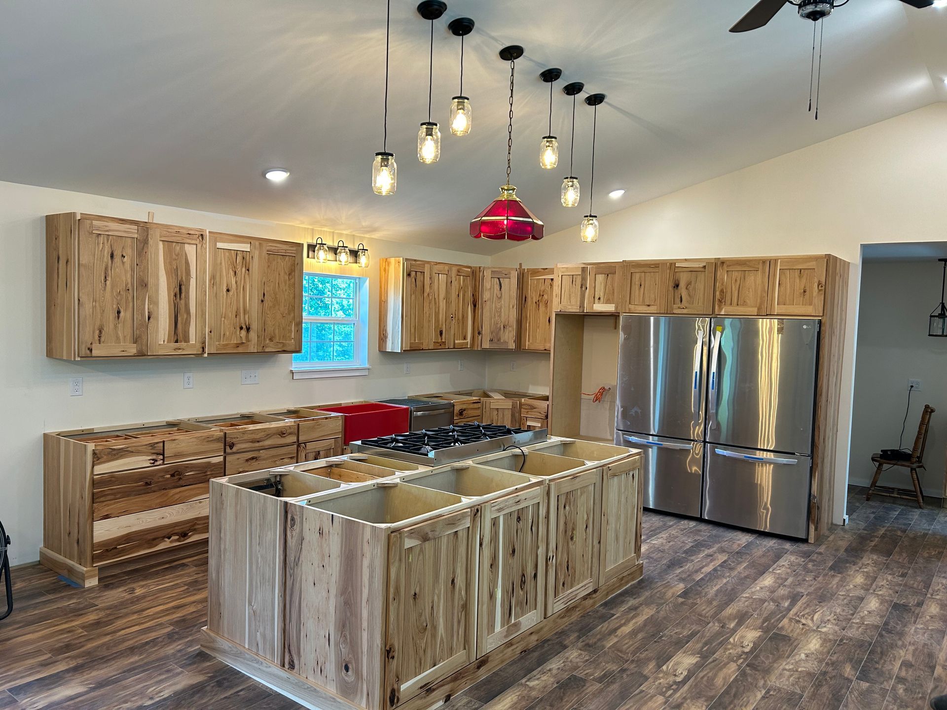 A kitchen under construction with rustic wooden cabinets, a central island, stainless steel appliances, and pendant lights.