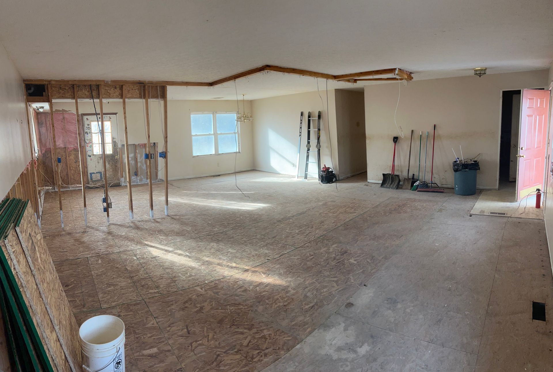 A large, open-concept room under renovation with exposed wall studs, subflooring, and a partially removed ceiling.