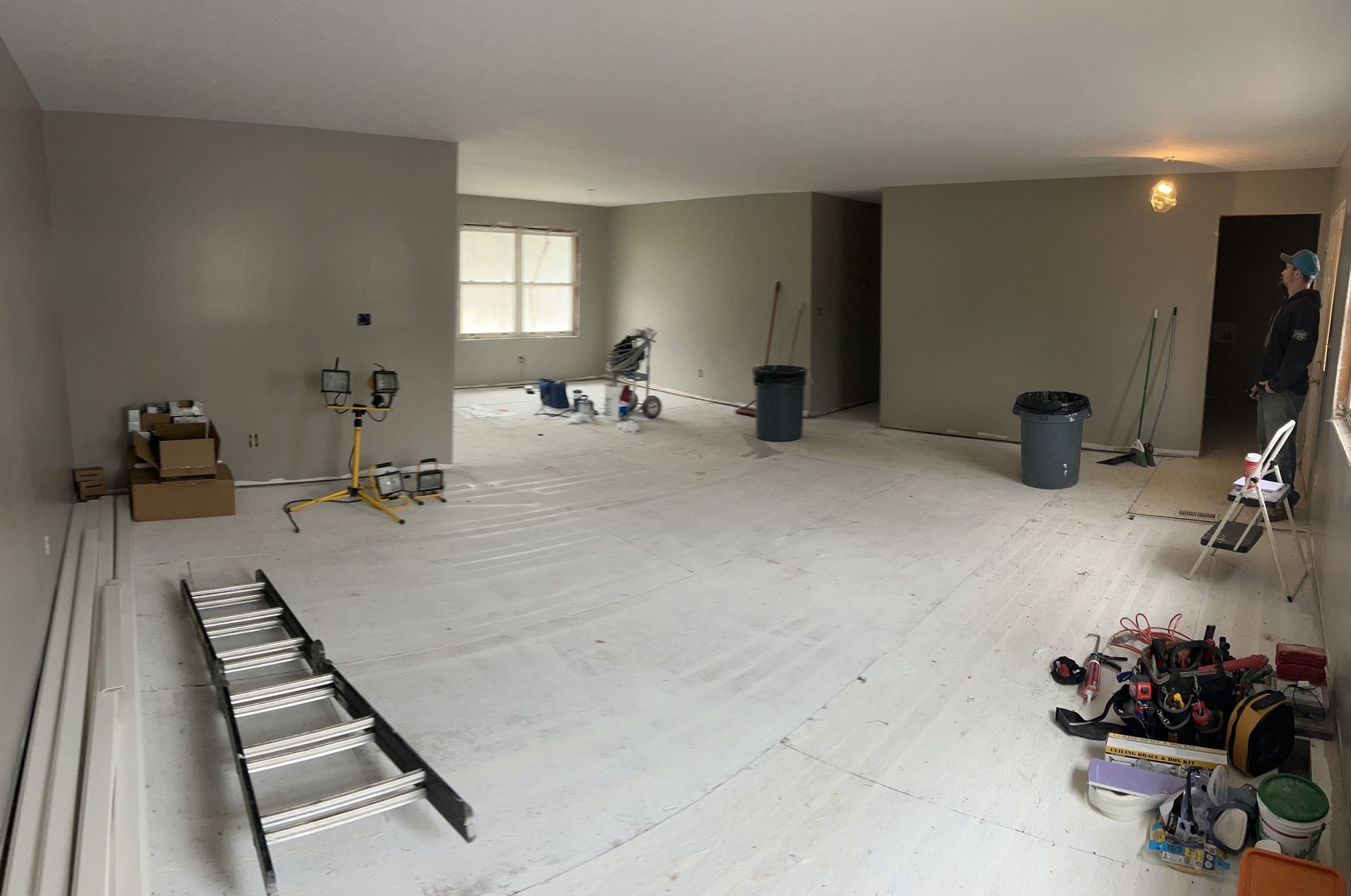 An interior shot of a spacious room under renovation with beige walls, a white floor covering, and construction equipment.