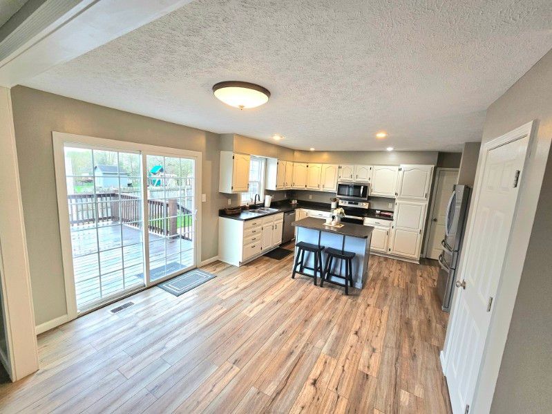 A kitchen with white cabinets, a central island with stools, and sliding glass doors leading to an outdoor deck.