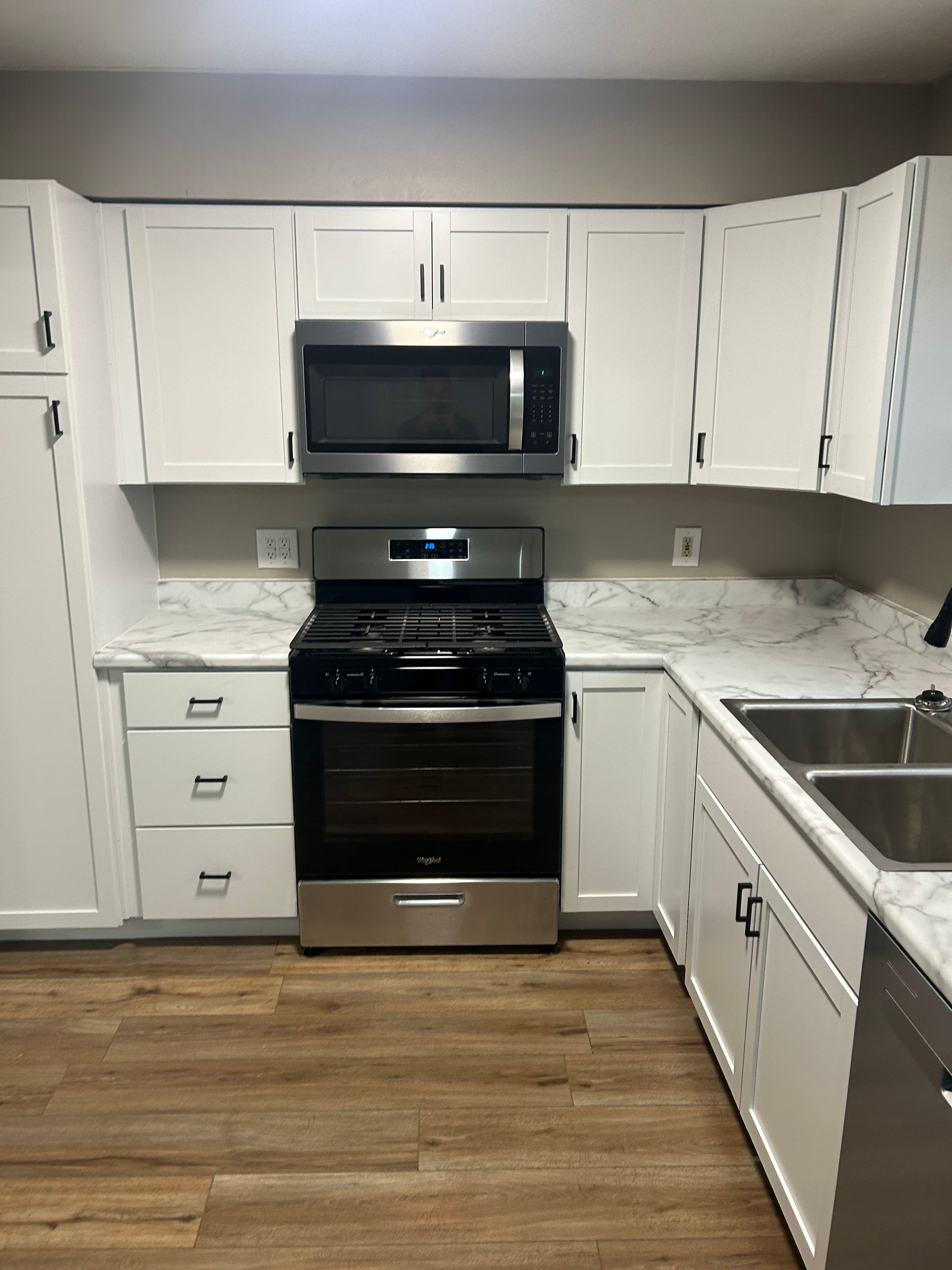 Modern kitchen with white cabinets, stainless steel appliances, marble-patterned countertops, and wood-look flooring.