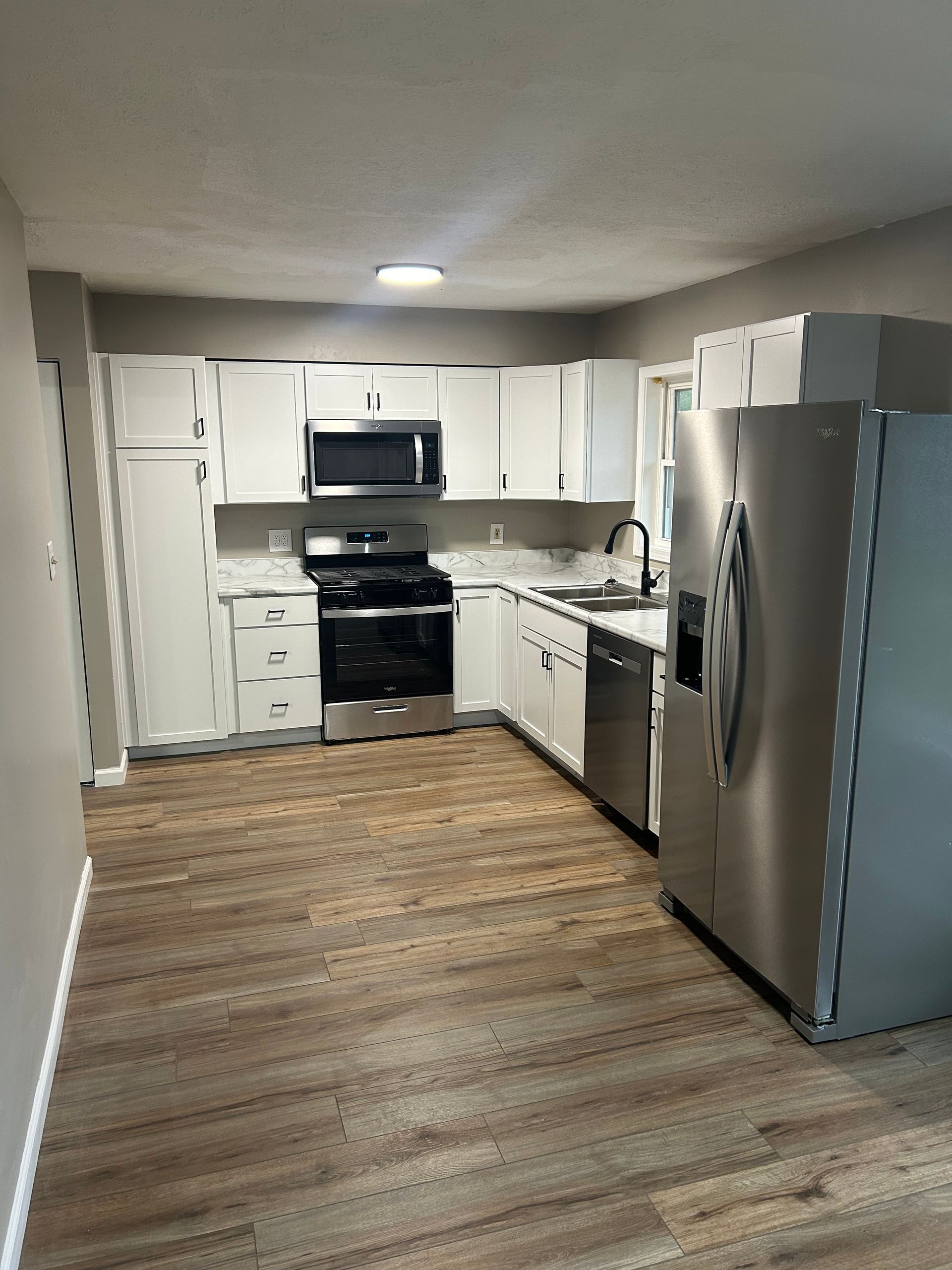 A kitchen featuring white cabinets, stainless steel appliances, a dark oven, and light wood-patterned flooring.