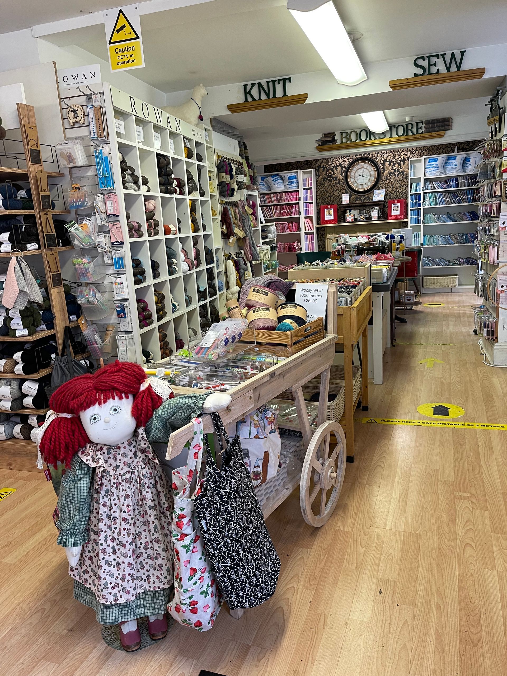 Craft store aisle with shelves of yarn, crafts, and a cart of handmade doll dresses