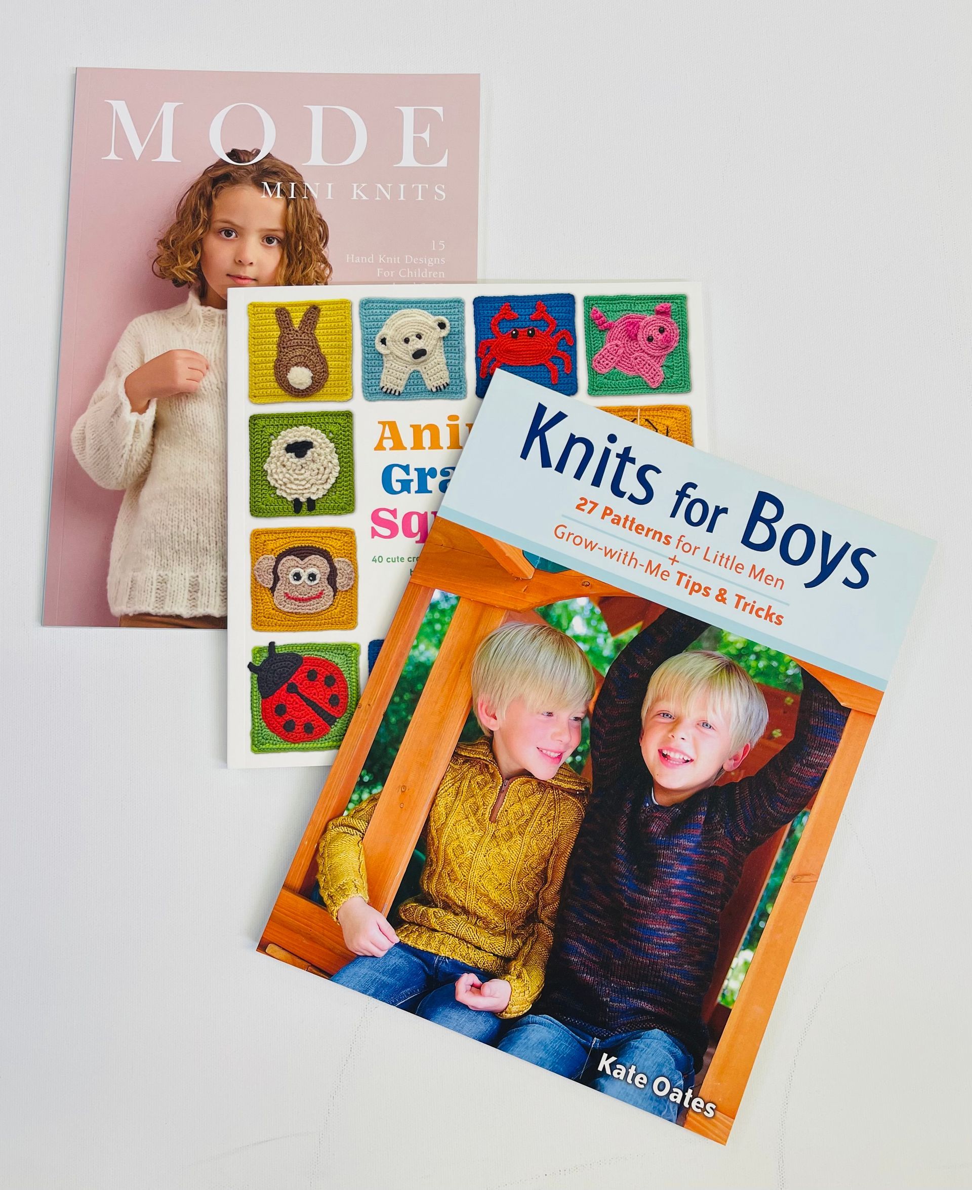 Three knitting books: Mode, Animal Granny Squares, Knits for Boys, arranged on a white surface.