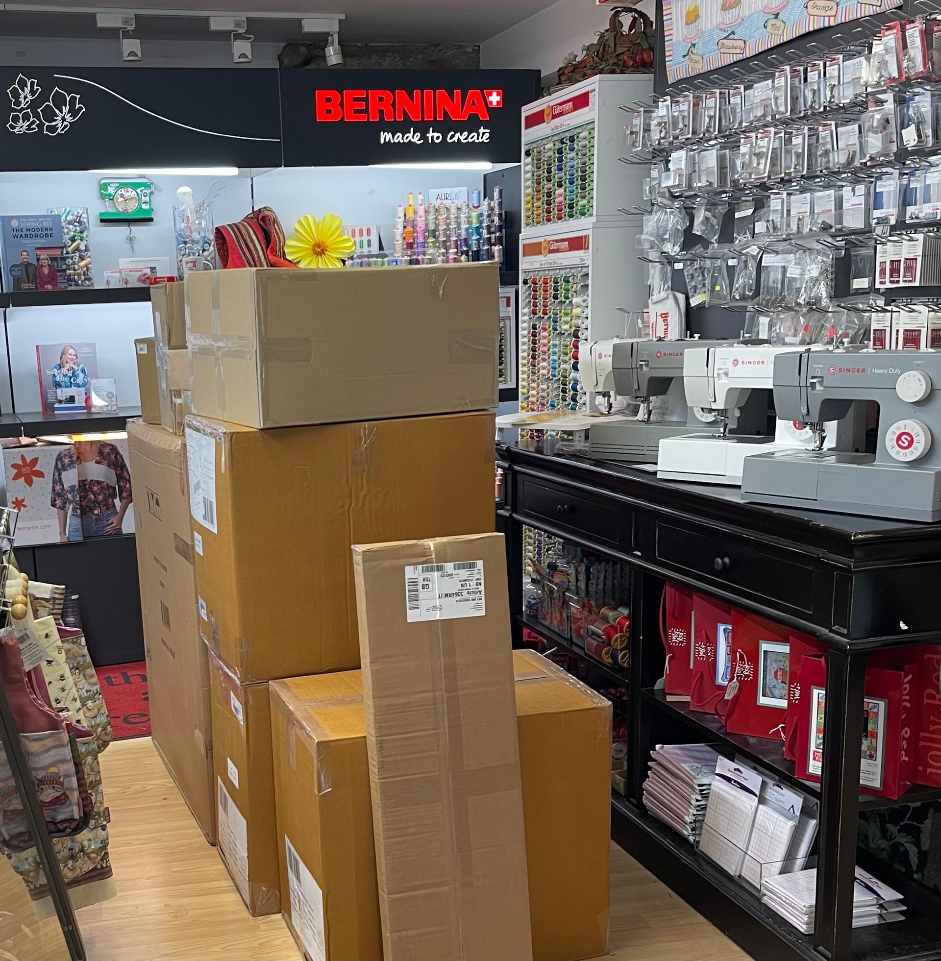 Boxes stacked near sewing machines in a sewing supply shop, Bernina sign, with sewing notions on display.