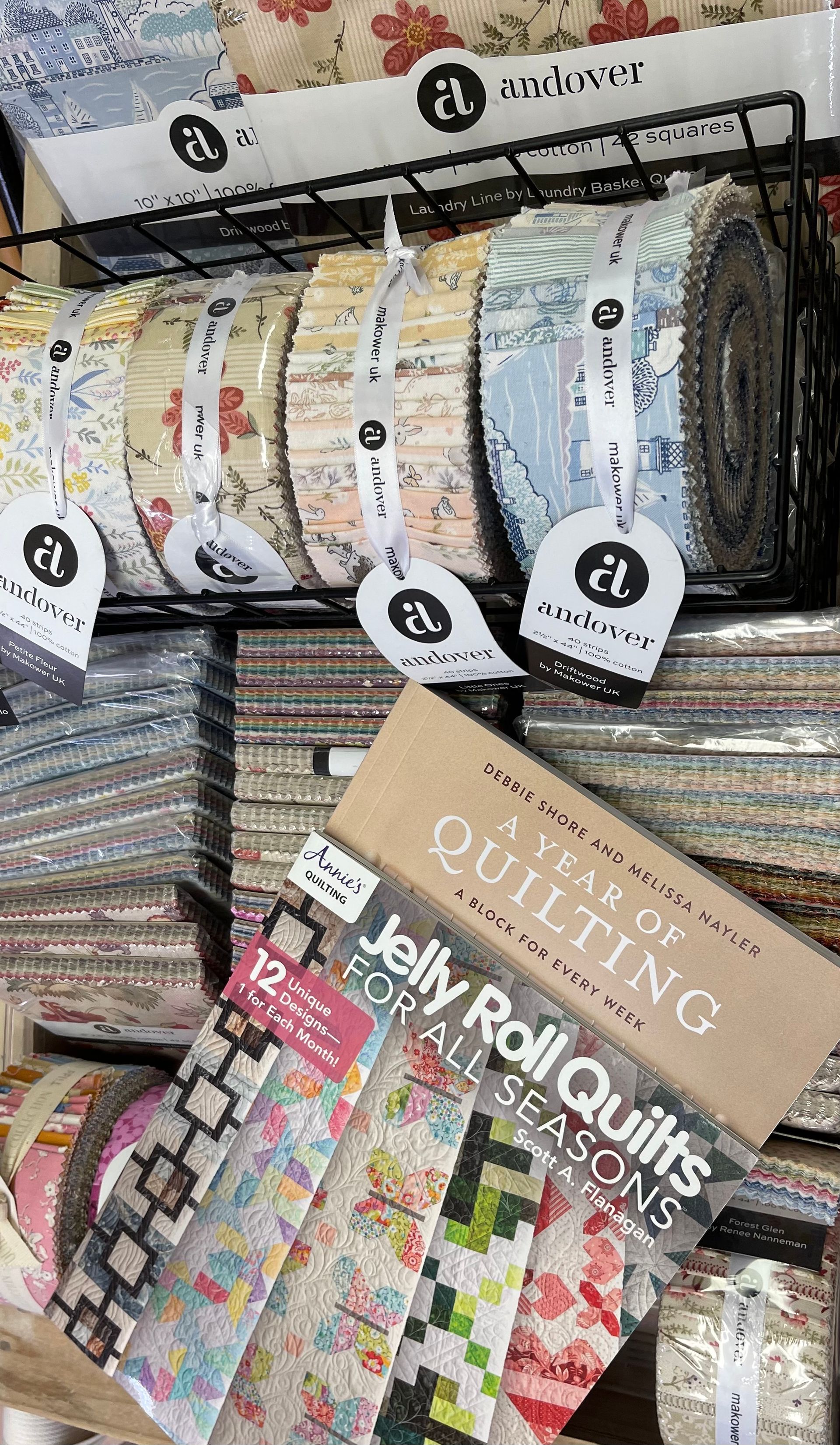 Stacked decorative fabric rolls and folded textile samples with colorful patterns on a display shelf.