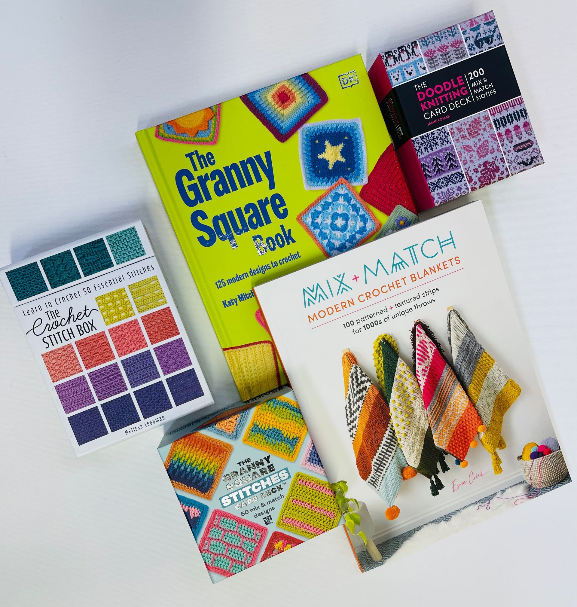 Assorted colorful embroidery pattern books arranged in a stack on a light background