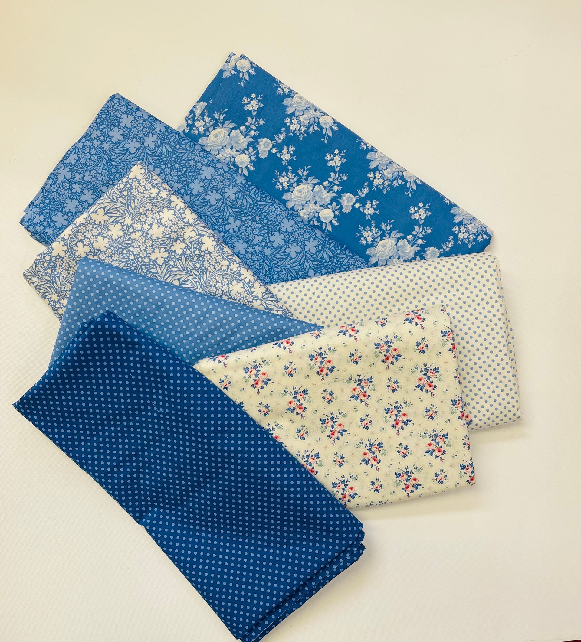 Assorted folded fabric swatches in blue, white, and cream floral and dotted patterns arranged in a fan.