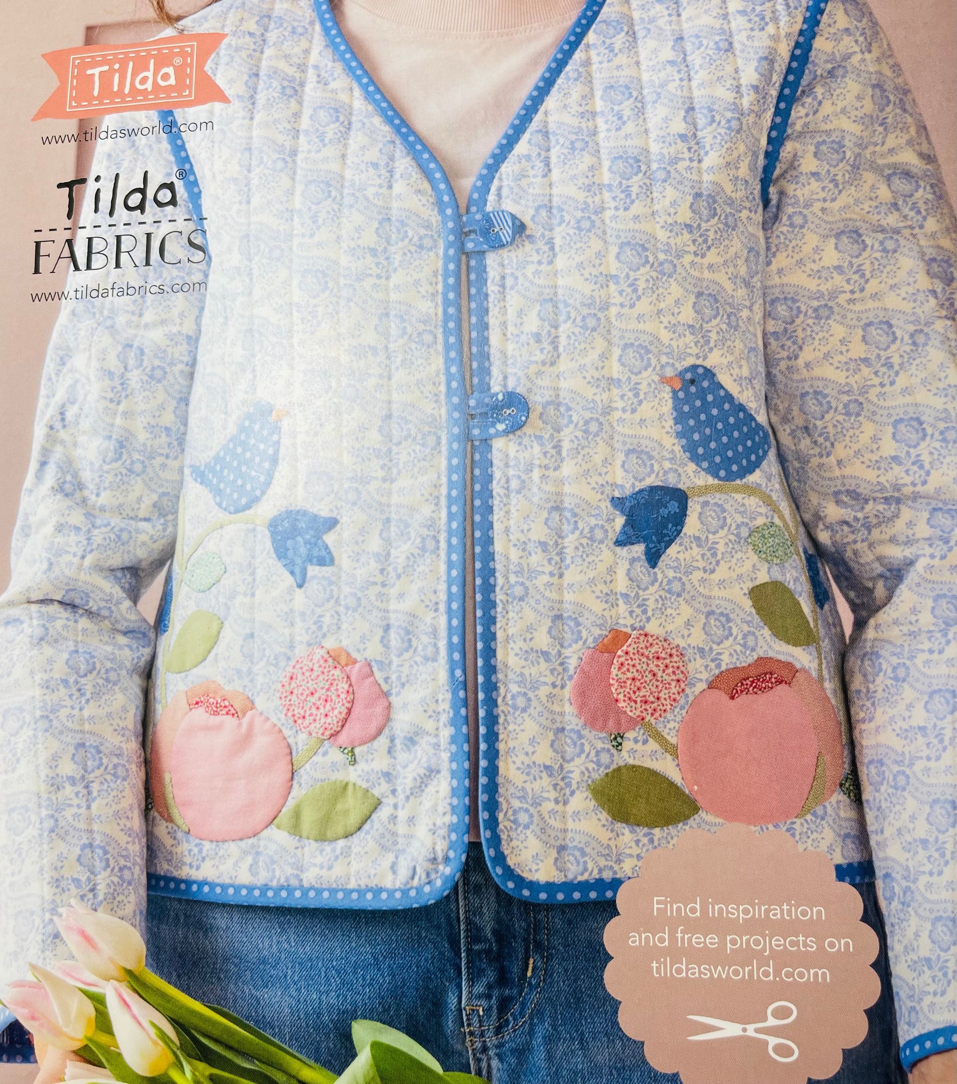 Floral quilted jacket with blue trim and pink flower embroidery, worn over blue jeans.