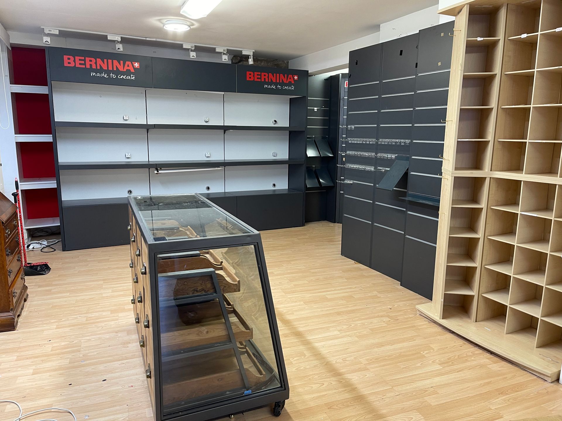 Empty retail display room with wall shelving, a central glass display case, and pegboard panels