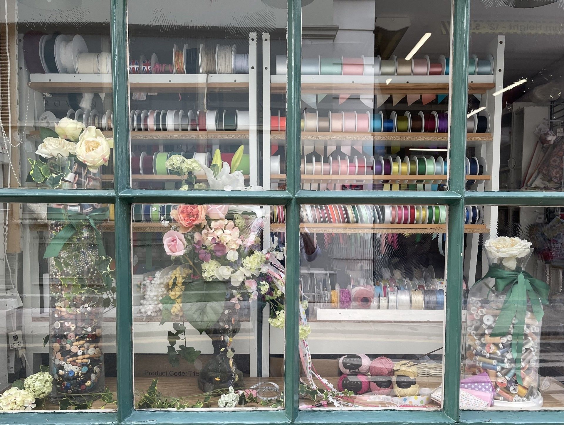 Craft shop window display with crafting supplies and spools of ribbon.