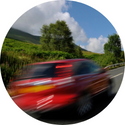 A red car is driving down a country road.