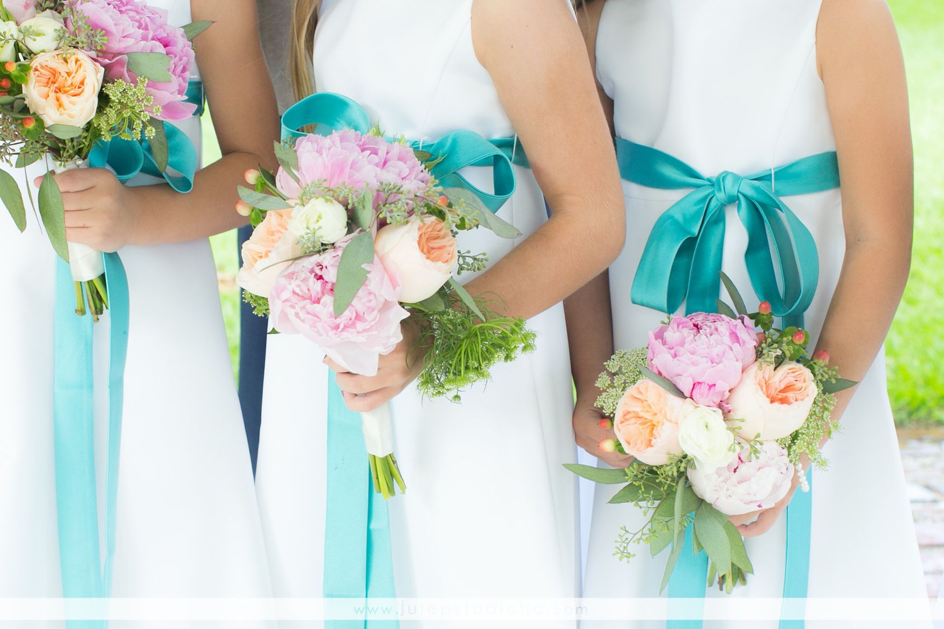 Bridesmaids holding bouquets of pink and peach flowers; white dresses with teal ribbon accents.