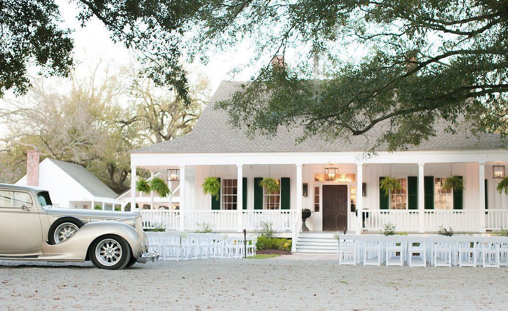 White house with porch and seating for an event; vintage car parked in the foreground.