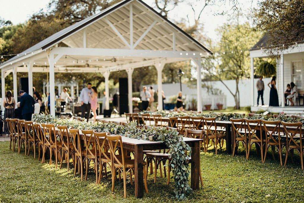 Outdoor wedding ceremony setup with rows of chairs, tables, and a white gazebo.