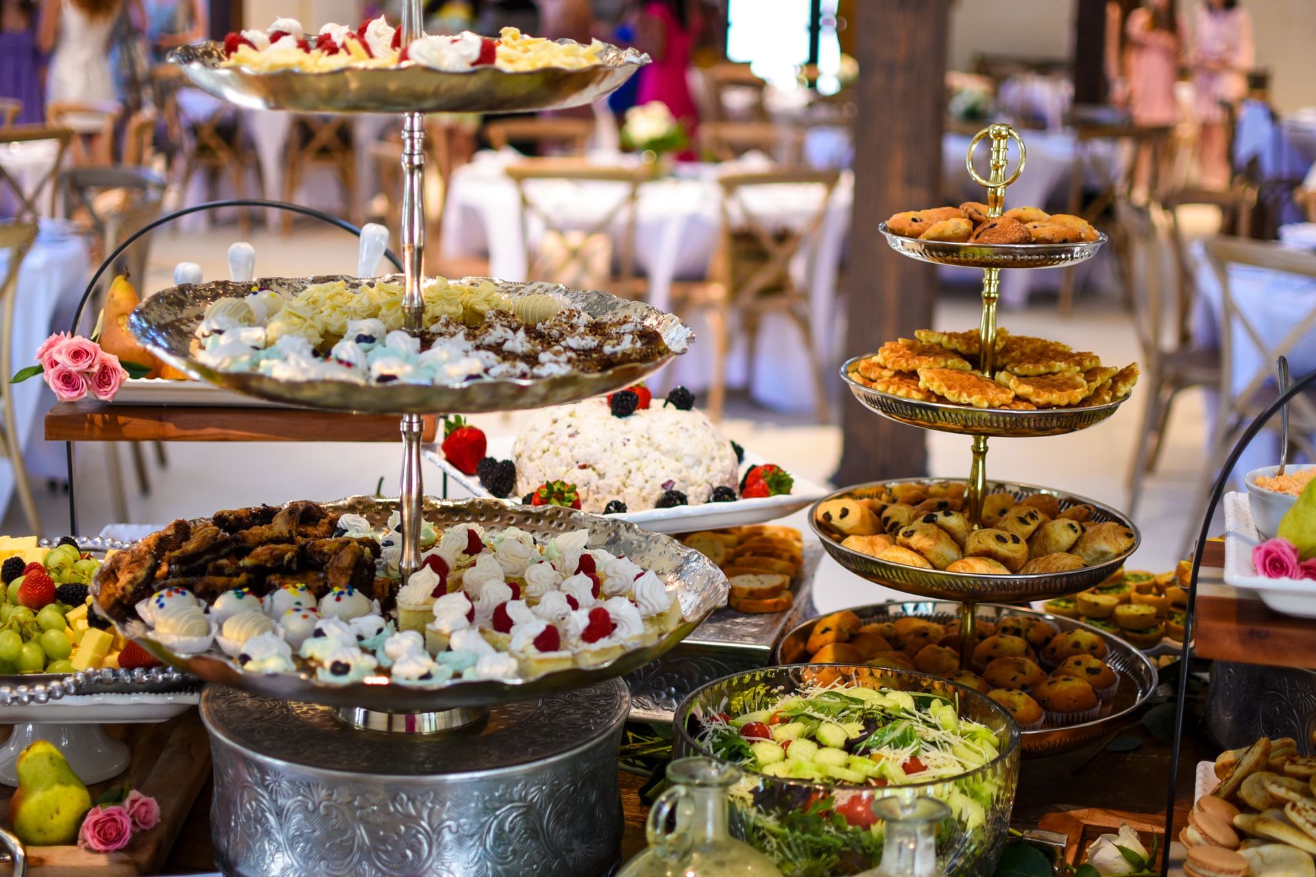 Dessert buffet with tiered trays of pastries, fruits, and salads; set at an event with tables and chairs.