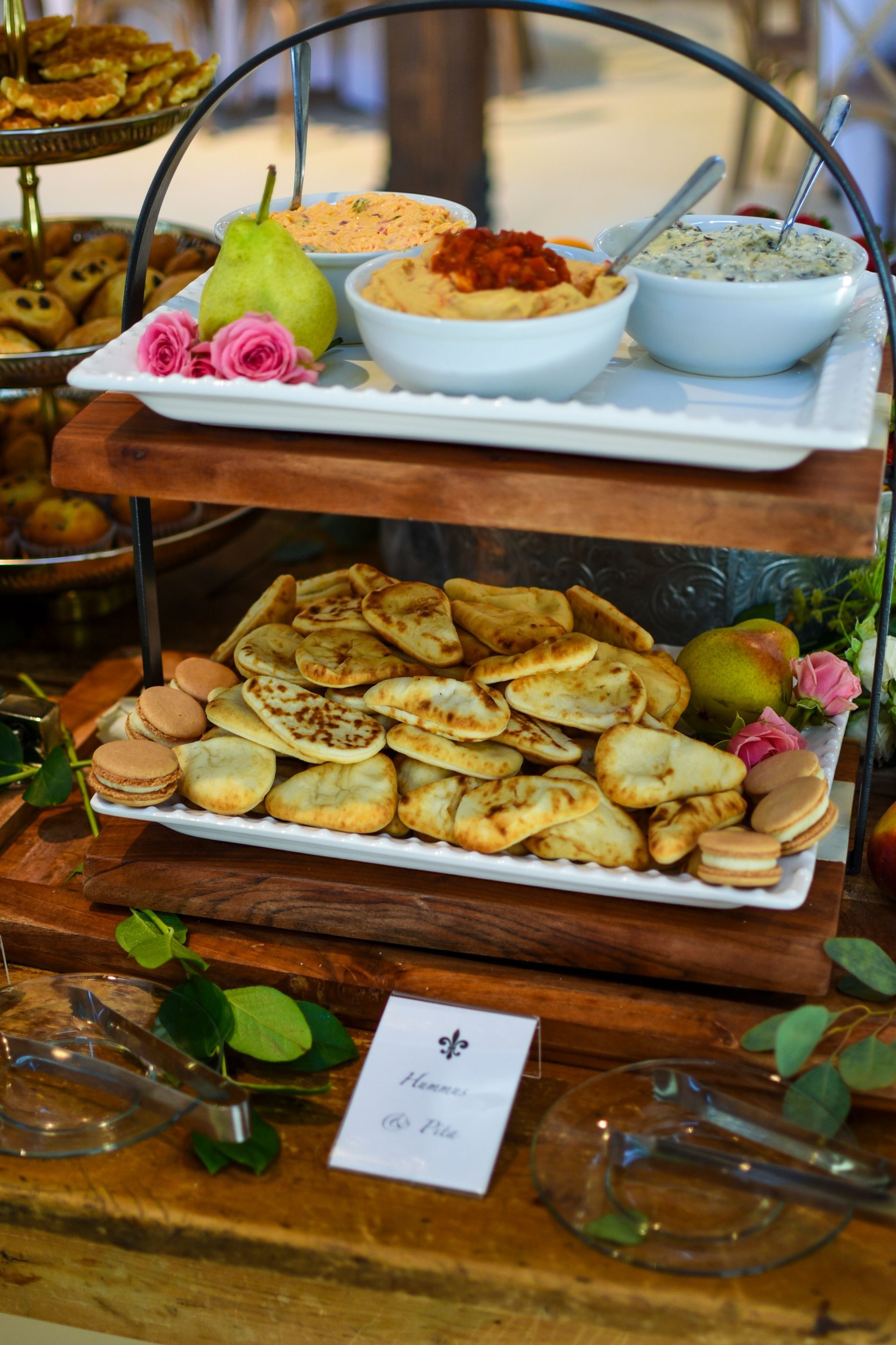 Tiered serving tray with dips, flatbreads, pears, and macarons on a wooden table.