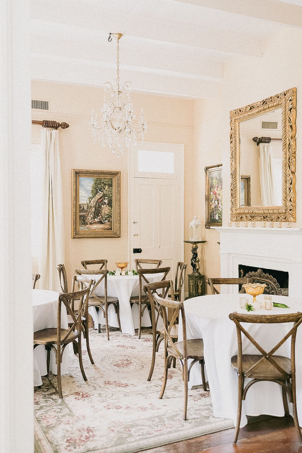 Elegant dining room with tables set for guests, chandelier, fireplace, ornate mirror.