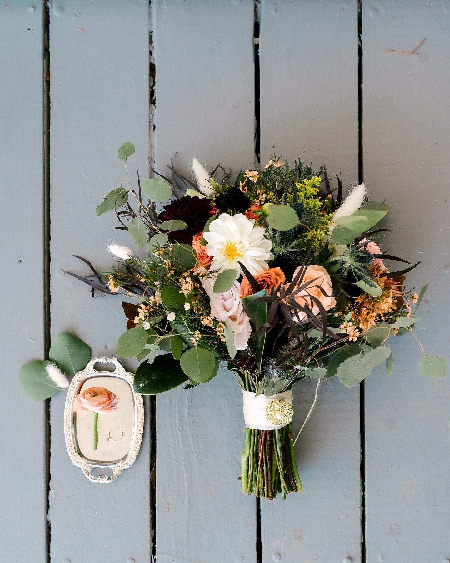 Wedding bouquet with white, peach, and green flowers, tied with a ribbon; small framed flower below.