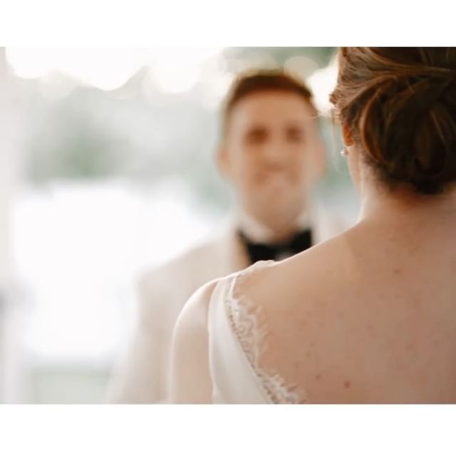 Bride and groom facing each other; groom blurred in the background, bride's back is in focus, at a wedding.