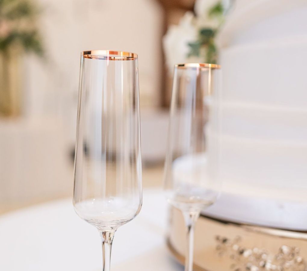 Two champagne flutes with gold rims next to a white cake, wedding setting.