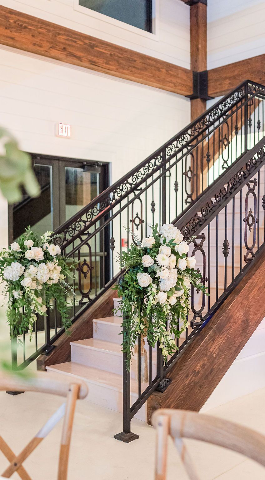 Staircase with ornate black railing, decorated with white flowers and greenery.