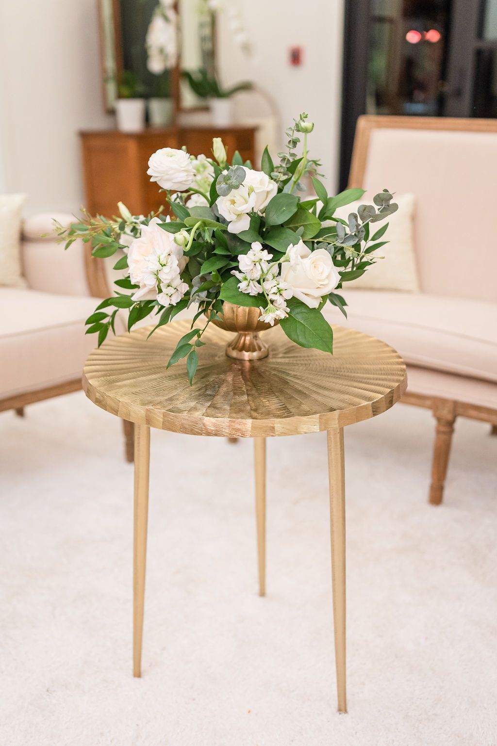 Gold side table with white floral arrangement, near beige seating.