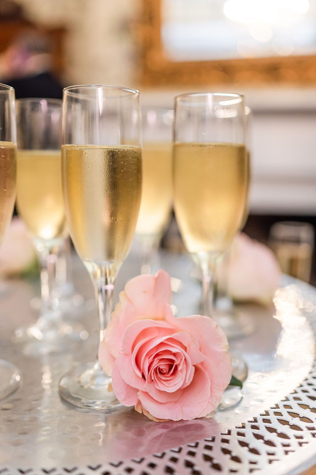 Champagne flutes filled with sparkling wine, next to a pink rose on a silver tray.