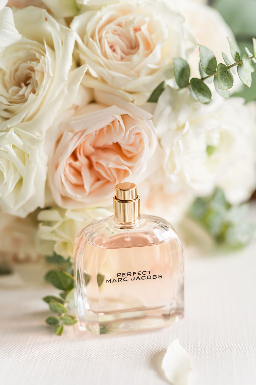 Perfume bottle in front of a bouquet of white and peach roses.