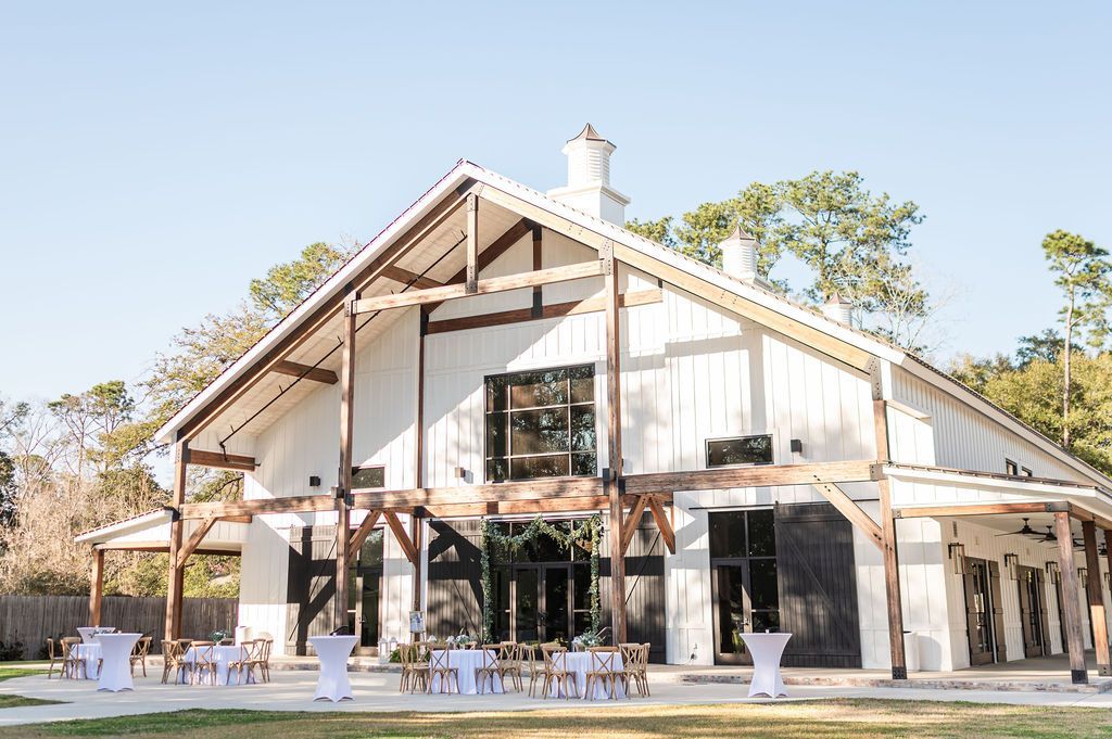 White barn venue with wooden accents, large windows, and outdoor seating.