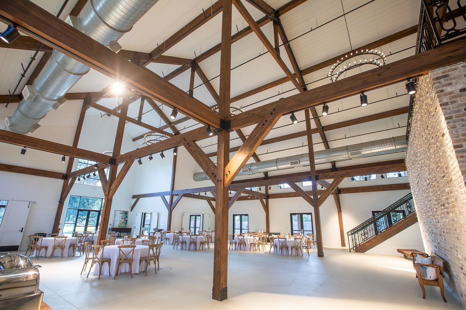 Large event space with exposed wooden beams, tables set for a gathering, and a staircase.